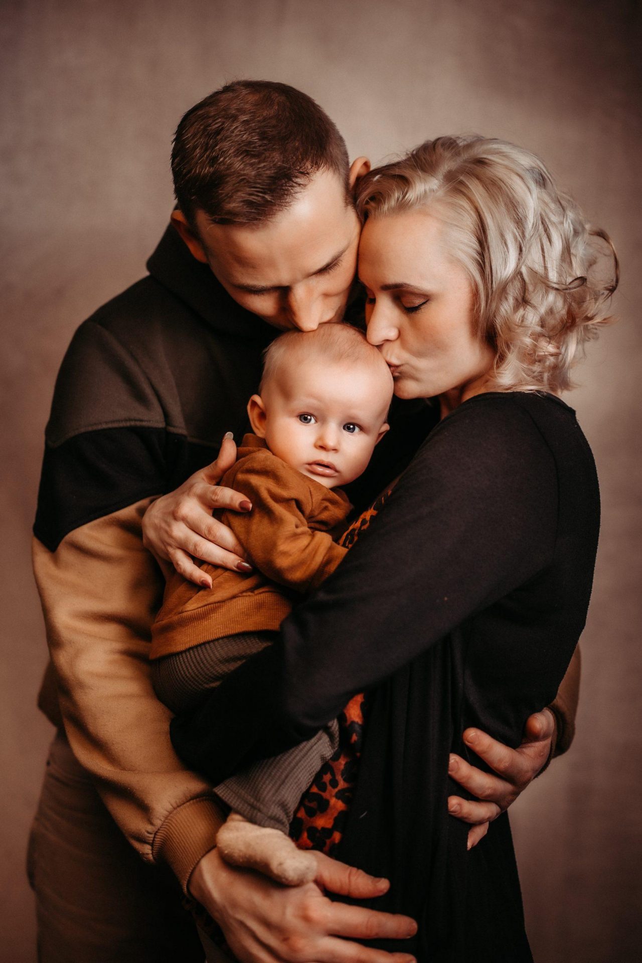 Die jungen Eltern küssen auf den Kopf des Babys