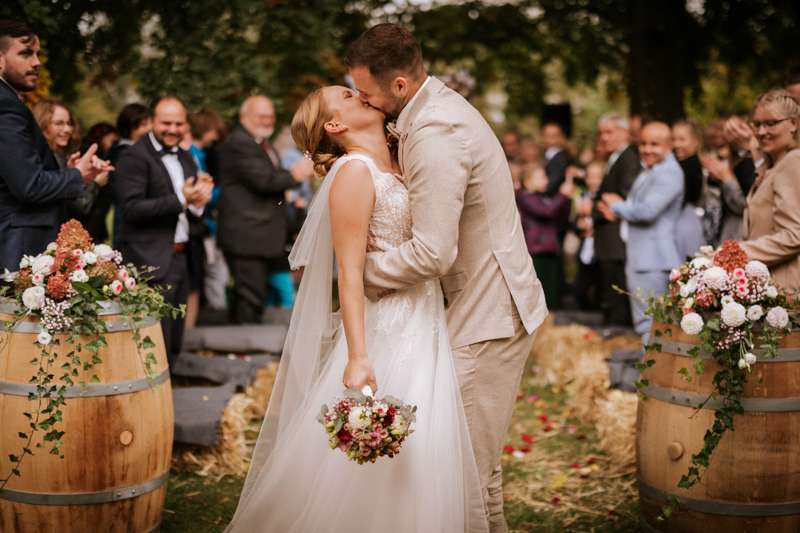 Route und Bräutigam küssen sich innig während im Hintergrund die Hochzeitsgäste applaudieren