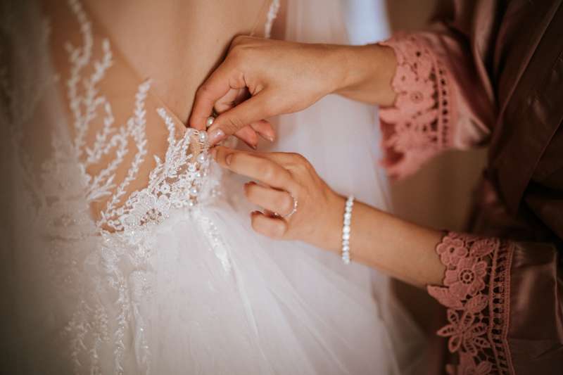 Die Braut kommt die kleinen Perlenköpfe des Brautkleides zugeknöpft