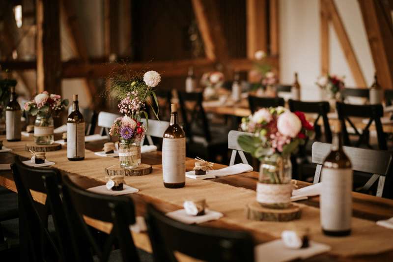 Rustikal geschmückte Hochzeitstafel mit Getränkekarten auf Weinflaschen und Vasen mit Wiesenblumen